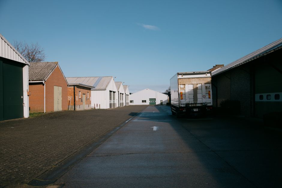 Narrow asphalt road with truck going between logistic buildings cottages in suburb area against blue sky in countryside in sunny day